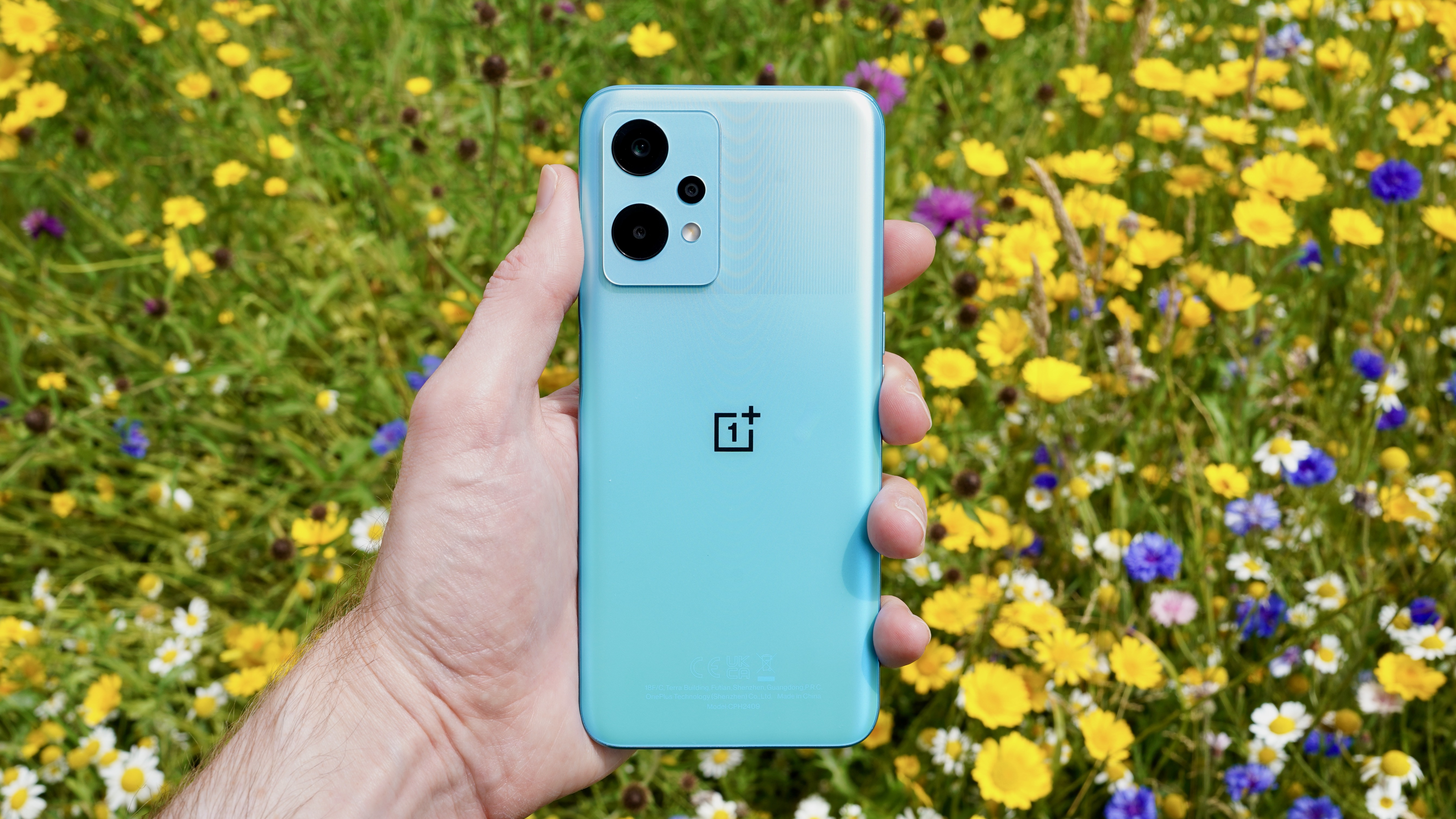 A hand holding the OnePlus Nord CE 2 Lite in a field showing the rear of the phone