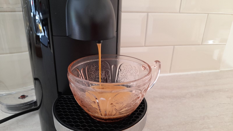 The Vertuo Plus is dispensing a stream of coffee into a cup
